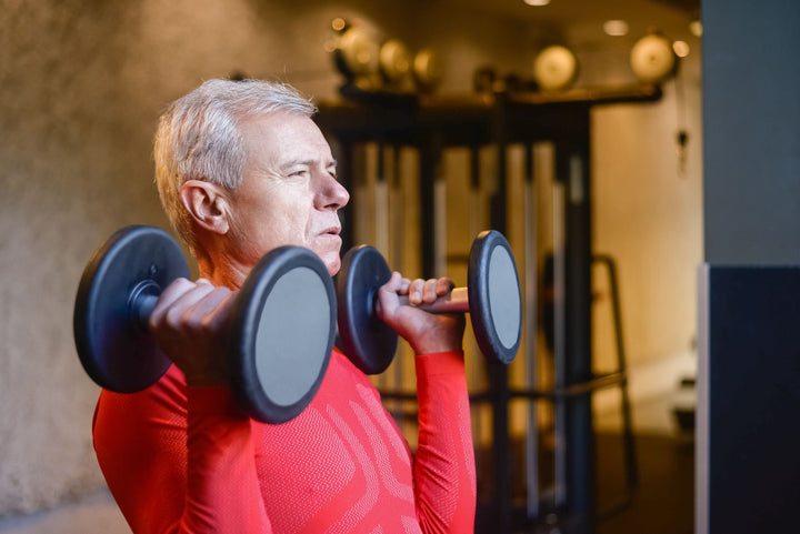 Hombre adulto mayor levantando mancuernas en el gym, mostrando fuerza y vitalidad después de los 40 años